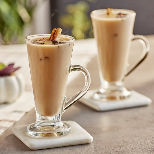 A glass mug of Capora Chai Tea Latte with a cinnamon stick in it.