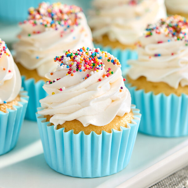 A vanilla cupcake with white frosting and colorful sprinkles in a blue paper liner.