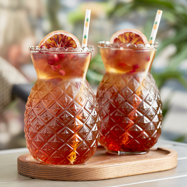 A glass pitcher of red Tiki energy drink with two glasses on a tray, garnished with orange slices.