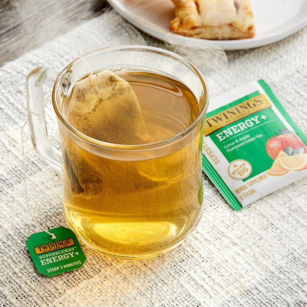 A glass mug of Twinings Superblends Energy+ Citrus & Apple Green Tea with a tea bag in it.