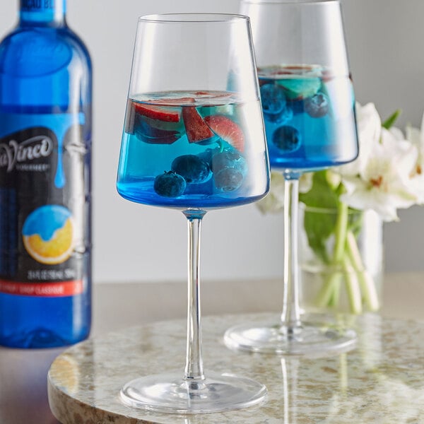Two wine glasses of blue liquid with fruit in it.