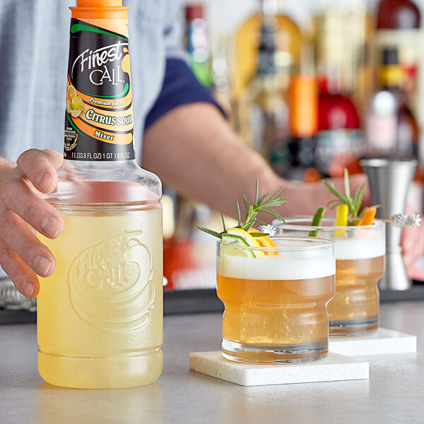 A bartender pouring Finest Call Premium Citrus Sour Mix into a glass on a table in a cocktail bar.