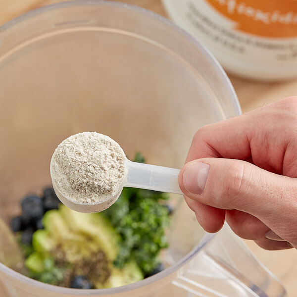 A hand holding a measuring spoon full of white Add A Scoop Antioxidant Blend powder.