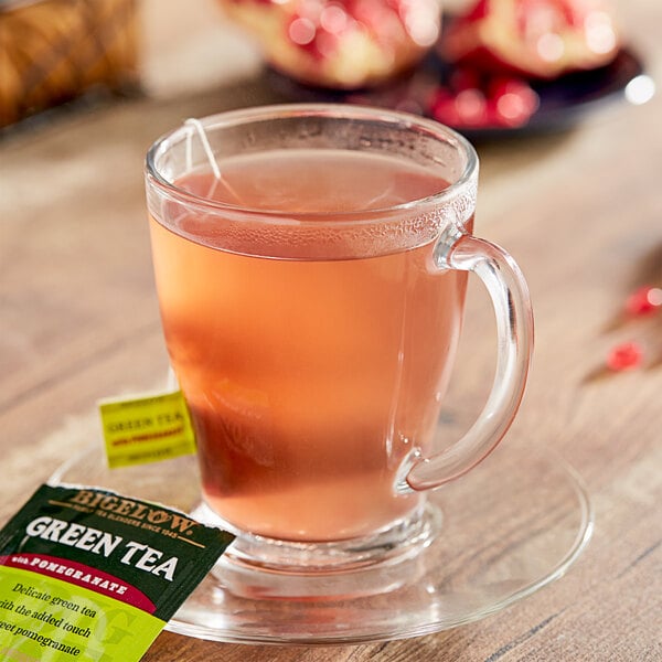 A glass cup of pink liquid with a Bigelow Green Tea with Pomegranate tea bag in it.