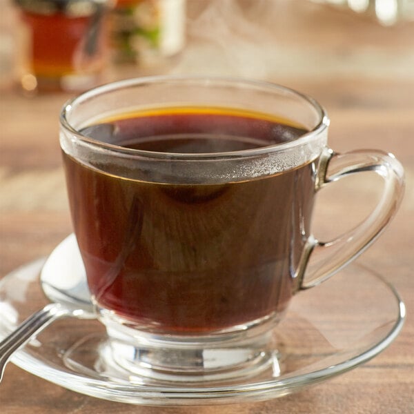 A glass cup of Bourbon Barrel Foods Bourbon Barrel Aged Whole Bean Coffee on a saucer with a spoon.