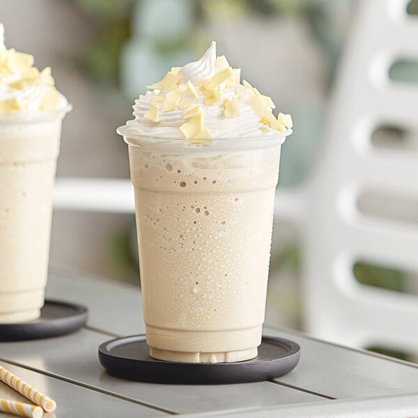 A white Capora frappe on a coaster with whipped cream and a straw.