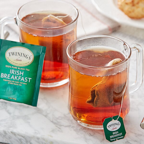 A glass mug and two mugs of Twinings Irish Breakfast Tea on a counter with a box of tea.