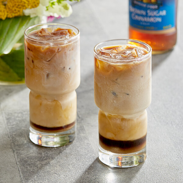 Two glasses of iced coffee and a bottle of Torani Sugar-Free Brown Sugar Cinnamon flavoring syrup.