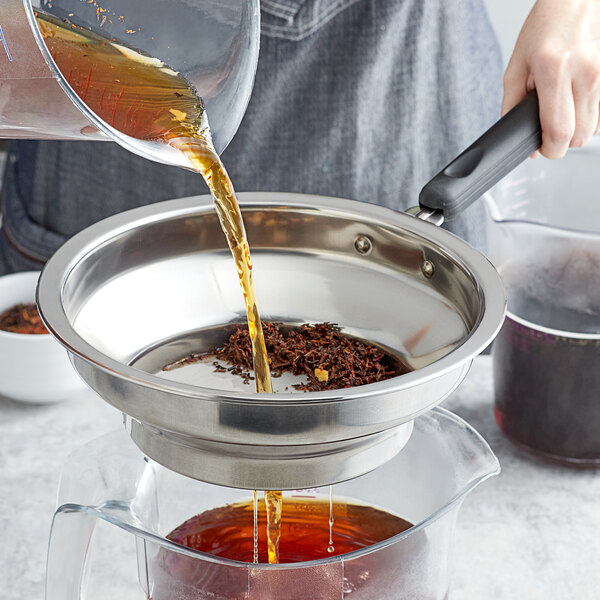 A person using a Bossen stainless steel tea filter to pour brown liquid into a glass.