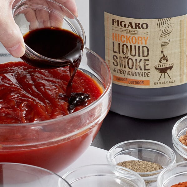 A person pouring Figaro hickory liquid smoke and marinade into a bowl.