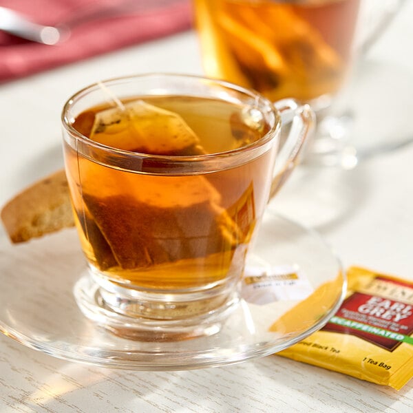 A glass cup of Twinings Earl Grey decaffeinated tea with a bag of tea on a saucer.