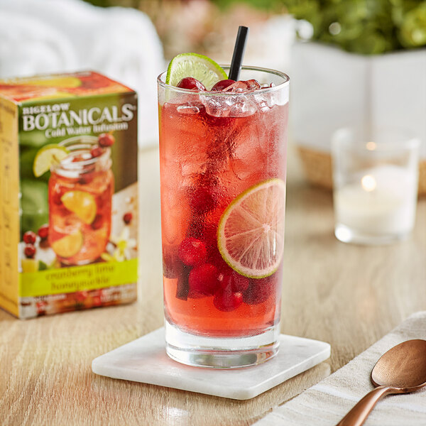 A glass of red Bigelow Cranberry Lime Honeysuckle tea with ice and fruit.