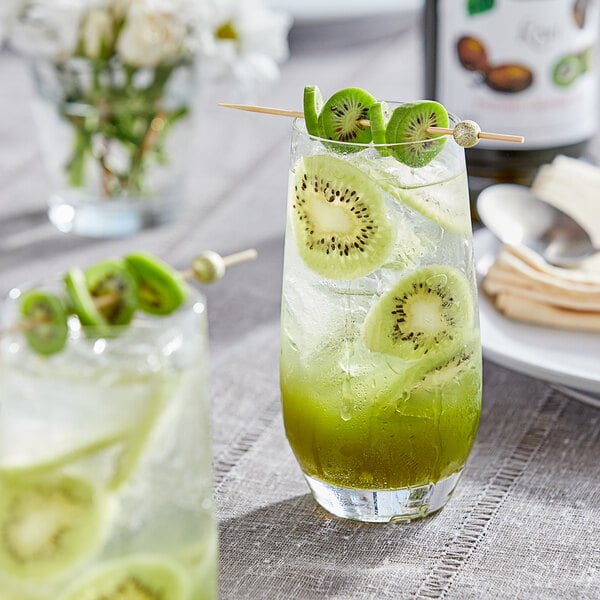 A glass of green drink with kiwi slices on top.