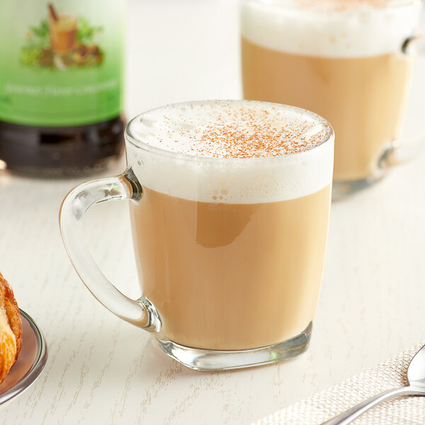 A table set with a glass mug of brown Monin Chai Tea on a table.
