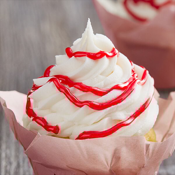 A cupcake with white frosting and red drizzle using Satin Ice Red Vanilla Glitter Glaze.