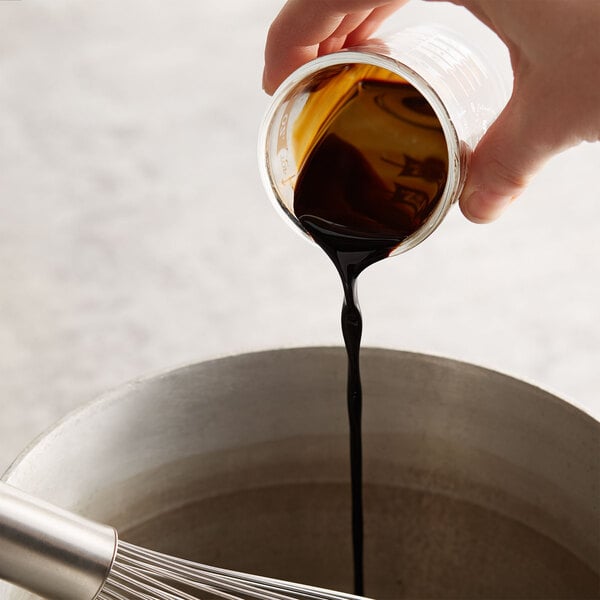 A person pouring Kitchen Bouquet browning sauce into a bowl.
