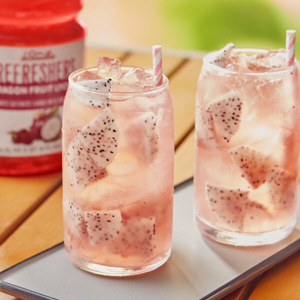 Two glasses of pink Dr. Smoothie dragon fruit refresher with a straw and dragon fruit.