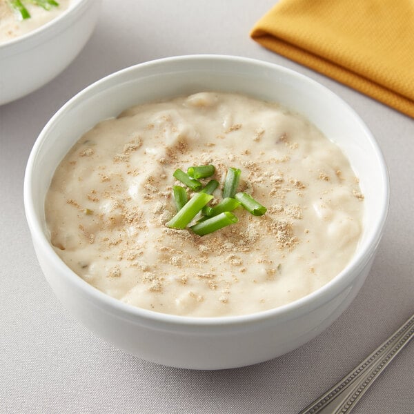 A bowl of soup with green onions and a spoon on the side.