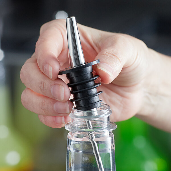 A person using a metal tip to pour Regal Cocktail Triple Sec syrup into a glass bottle.