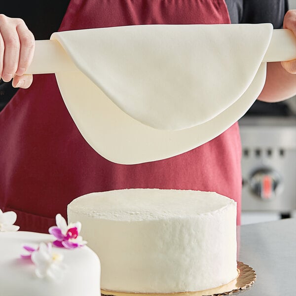 A person using Satin Ice Tropical White rolled fondant to decorate a cake with flowers using a rolling pin.