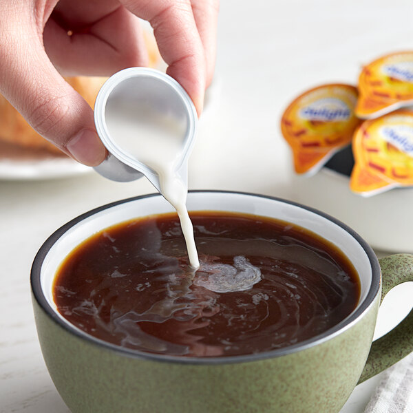 A person pouring International Delight Caramel Macchiato creamer into a cup of coffee.