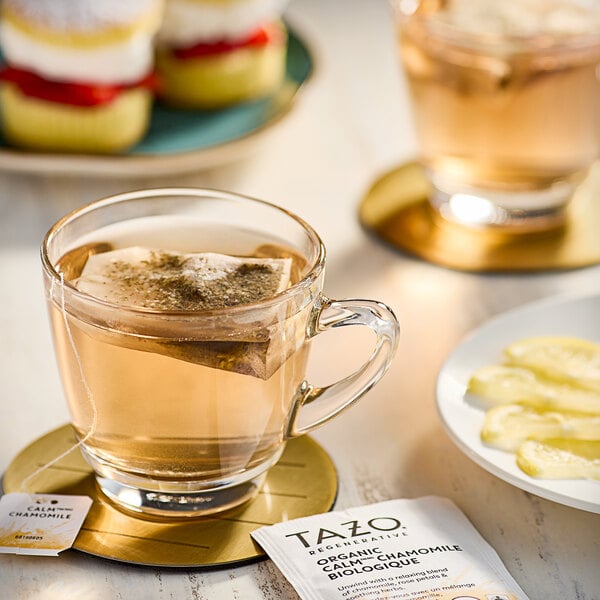 A glass cup of Tazo chamomile tea with a bag in it on a plate.