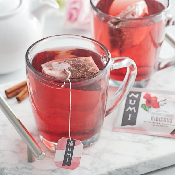 A glass mug of red Numi Organic Hibiscus tea with a tea bag in it.