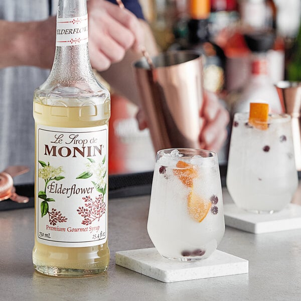 A bartender preparing a drink with Monin Premium Elderflower Flavoring Syrup on a table in a cocktail bar.