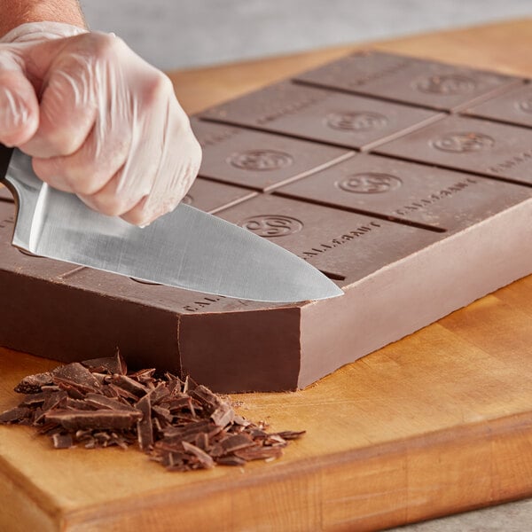 A person's gloved hand cutting Callebaut dark chocolate with a knife.