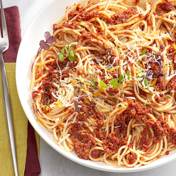 A bowl of spaghetti with sauce and red bell pepper granules.