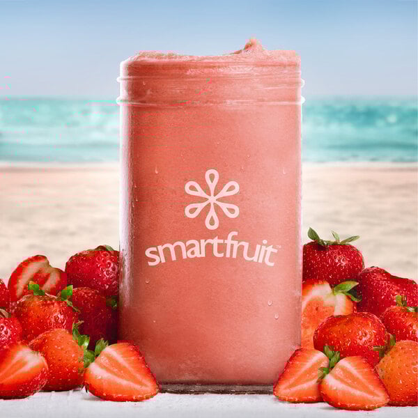 A pink strawberry smoothie in front of a beach with a Smartfruit Summer Strawberry Puree container.