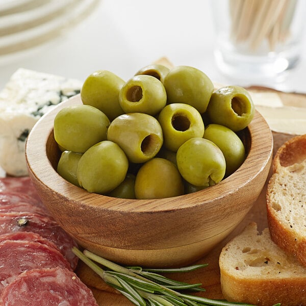 A bowl of Frutto d'Italia pitted green olives on a table with bread and meat.