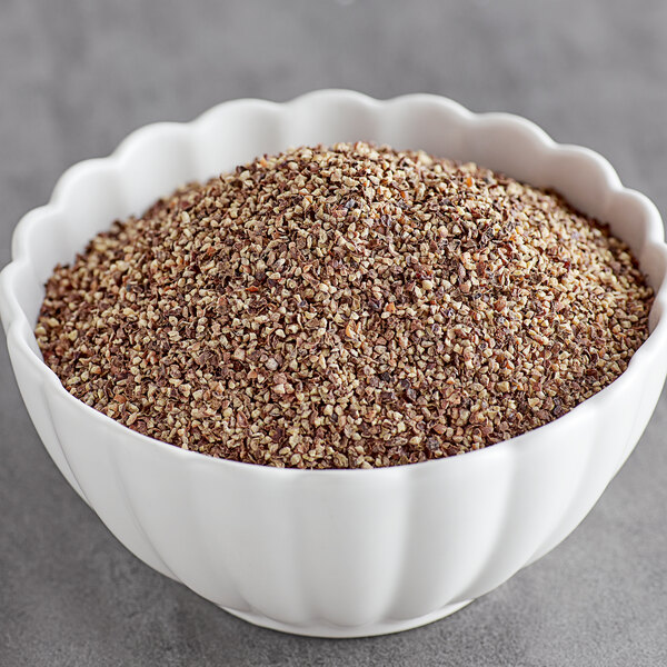 A case of Regal Butcher Grind Black Pepper on a gray surface with brown and white grains in a bowl.