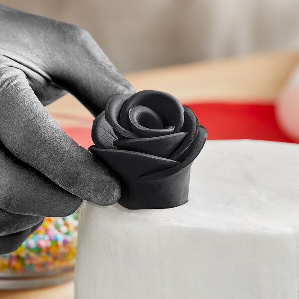 A hand holding a black rose made of Satin Ice black gum paste on a white cake.
