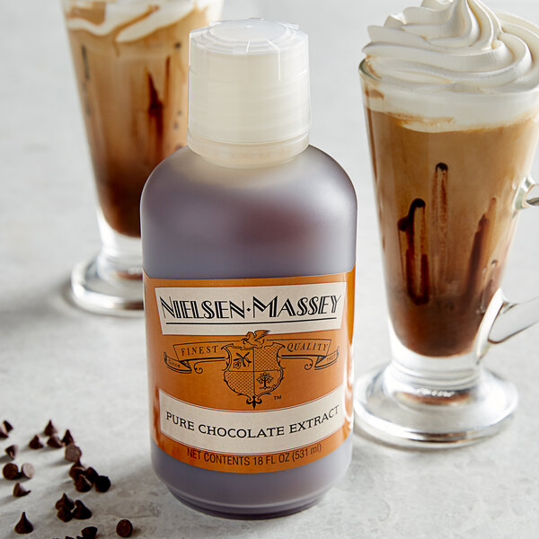 A bottle of Nielsen-Massey Pure Chocolate Extract next to a glass of chocolate liquid.