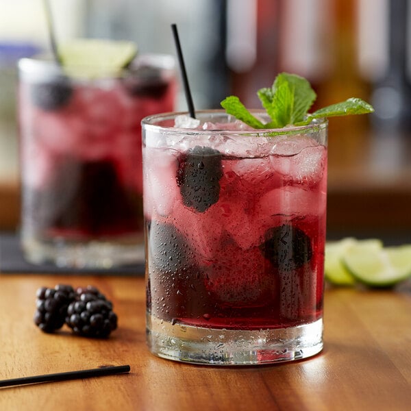A glass of red liquid flavored with Monin Wild Blackberry Syrup and garnished with berries and ice.