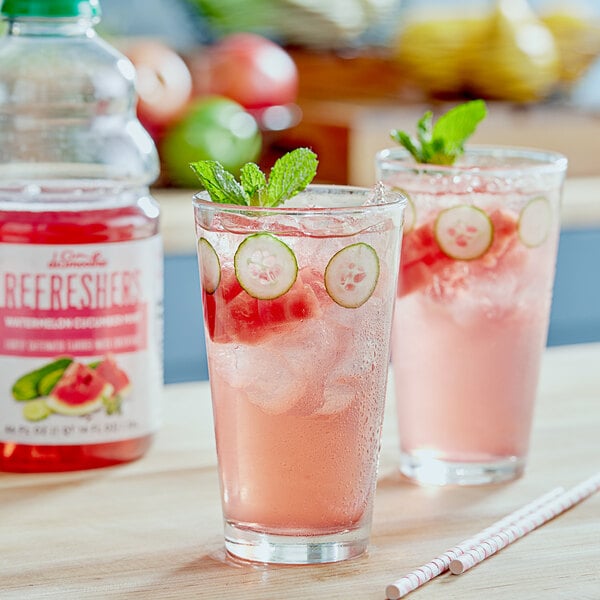 A glass of pink Dr. Smoothie Watermelon Cucumber Mint Refresher with cucumber slices and mint leaves.