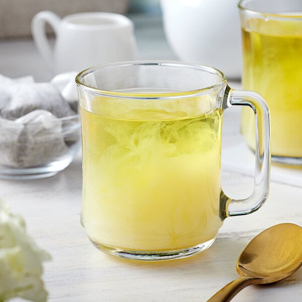 Two glass mugs filled with yellow liquid on a white background with a gold spoon.