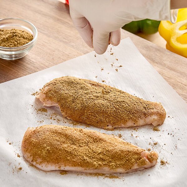 A person sprinkling Regal Big Flavor BBQ Rub seasoning on raw chicken breasts.
