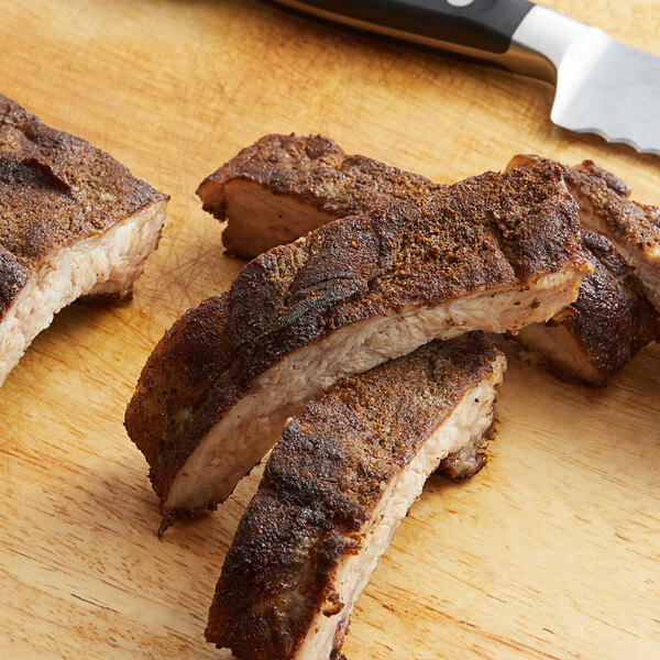 Regal Big Flavor BBQ Rub Seasoning next to a cutting board with pieces of meat and a knife.