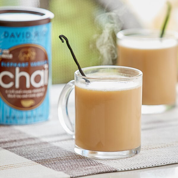 A glass mug of brown David Rio Elephant Vanilla Chai tea on a table with a can of chai.