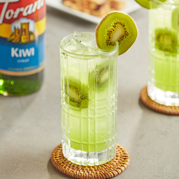 A glass of green kiwi drink with kiwi slices.