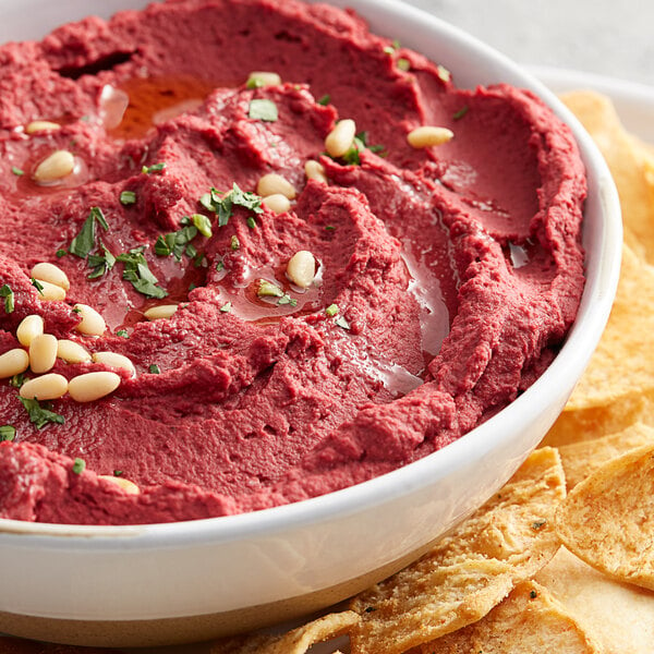 A bowl of beetroot hummus with chips.