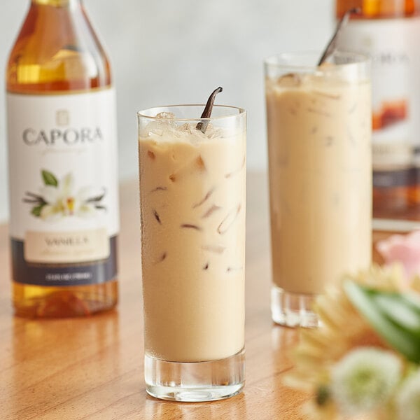 Two glasses of iced coffee on a table with Capora Vanilla Flavoring Syrup bottles.