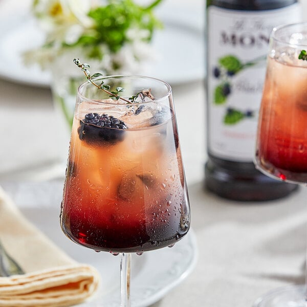 A glass of red liquid with ice and Monin Premium Blackberry Flavoring syrup with a blackberry garnish.