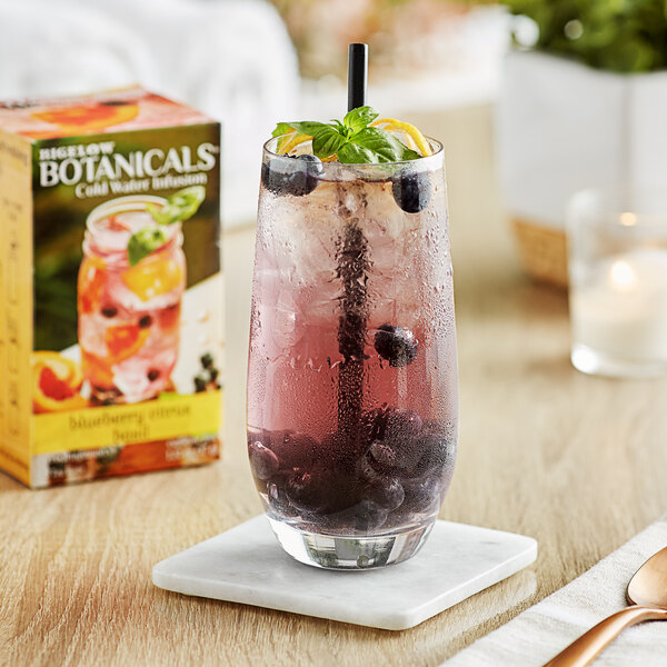 A glass of Bigelow Blueberry Citrus Basil cold water infusion with blueberries and a leaf next to a box of Bigelow Botanicals.