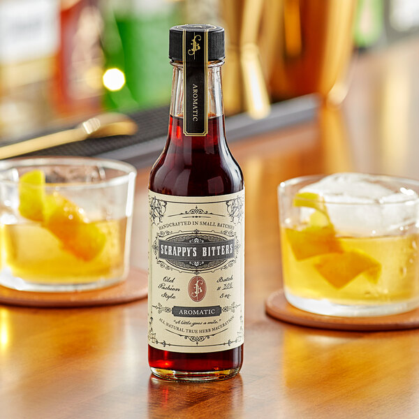 A bottle of Scrappy's Aromatic Bitters on a table with two drinks.