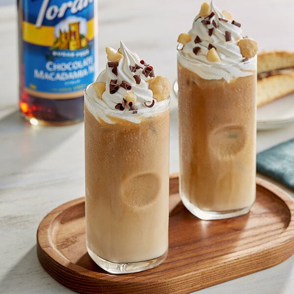 Two glasses of iced coffee with whipped cream and chocolate chips on a wooden tray on a table in a coffee shop.