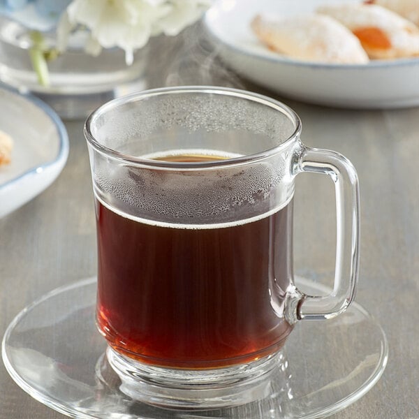 A glass mug of Caffe de Aroma Kona style coffee on a saucer with cookies.
