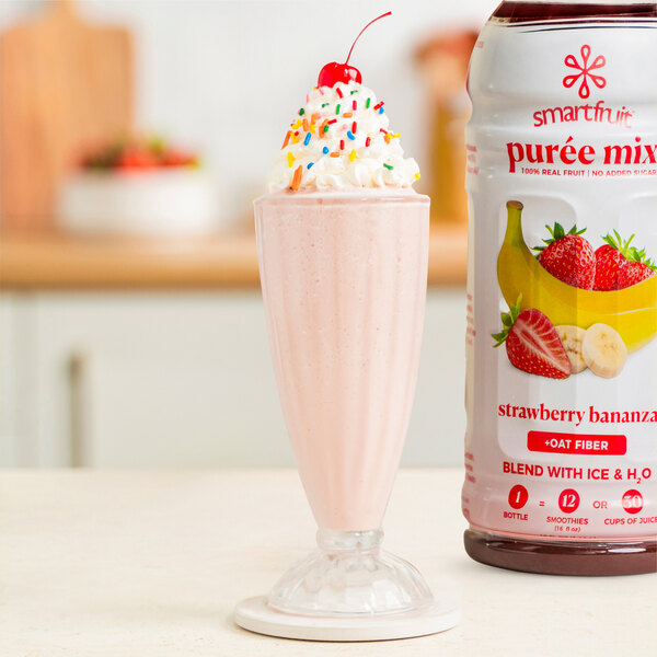 A pink Smartfruit Strawberry Bananza milkshake in a pink glass with whipped cream and sprinkles.